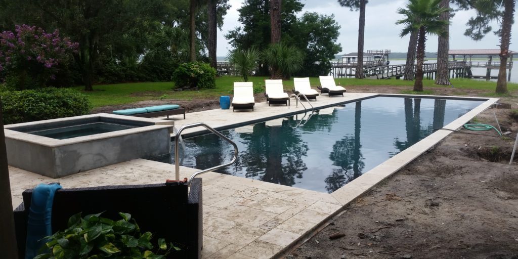 16x40 rectangle swimming pool with a raised spillover spa with a travertine swimming pool deck surface and matching coping stones