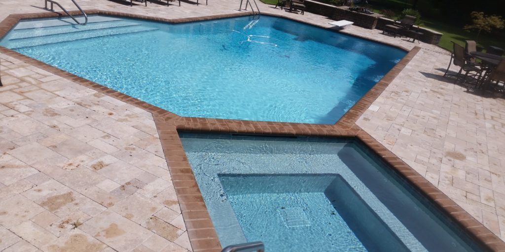 20x40 L-shaped pool with a 10' raised spillover spa with concrete bullnose brick and a travertine swimming pool deck surface